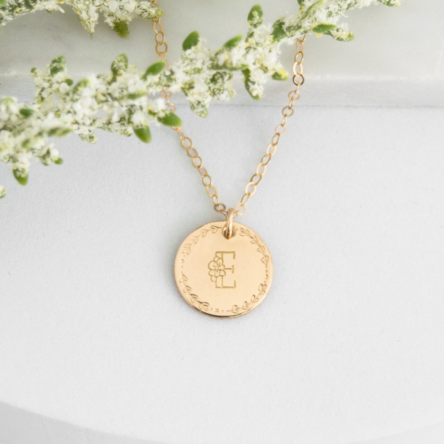 Flora Monogram Necklace featuring a floral initial and wreath design on a ½ inch disc, shown in gold.