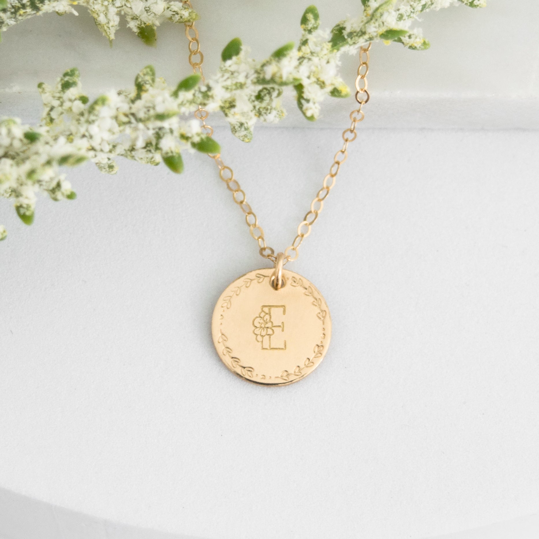Flora Monogram Necklace featuring a floral initial and wreath design on a ½ inch disc, shown in gold.
