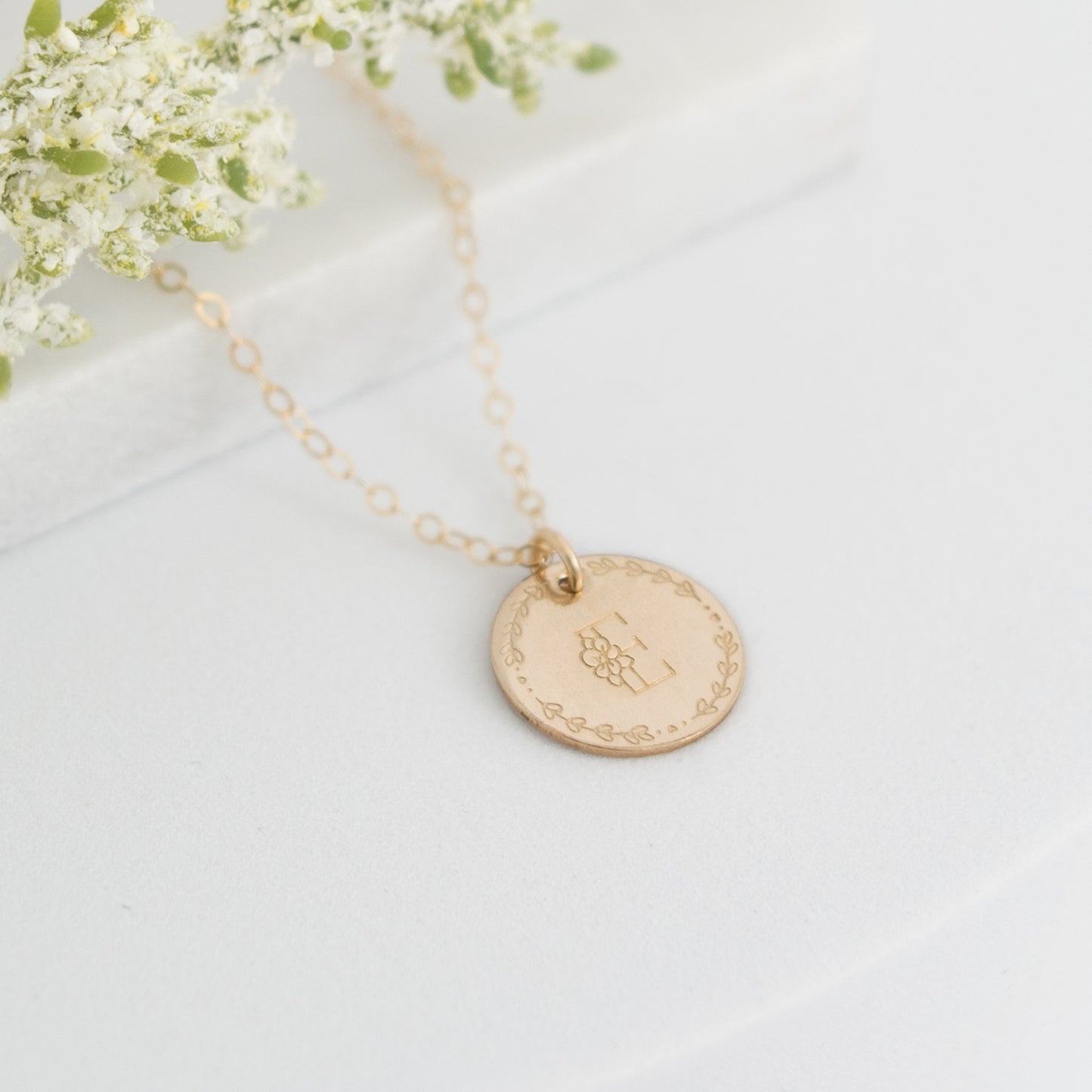 Flora Monogram Necklace featuring a floral initial and wreath design on a ½ inch disc, shown in gold.