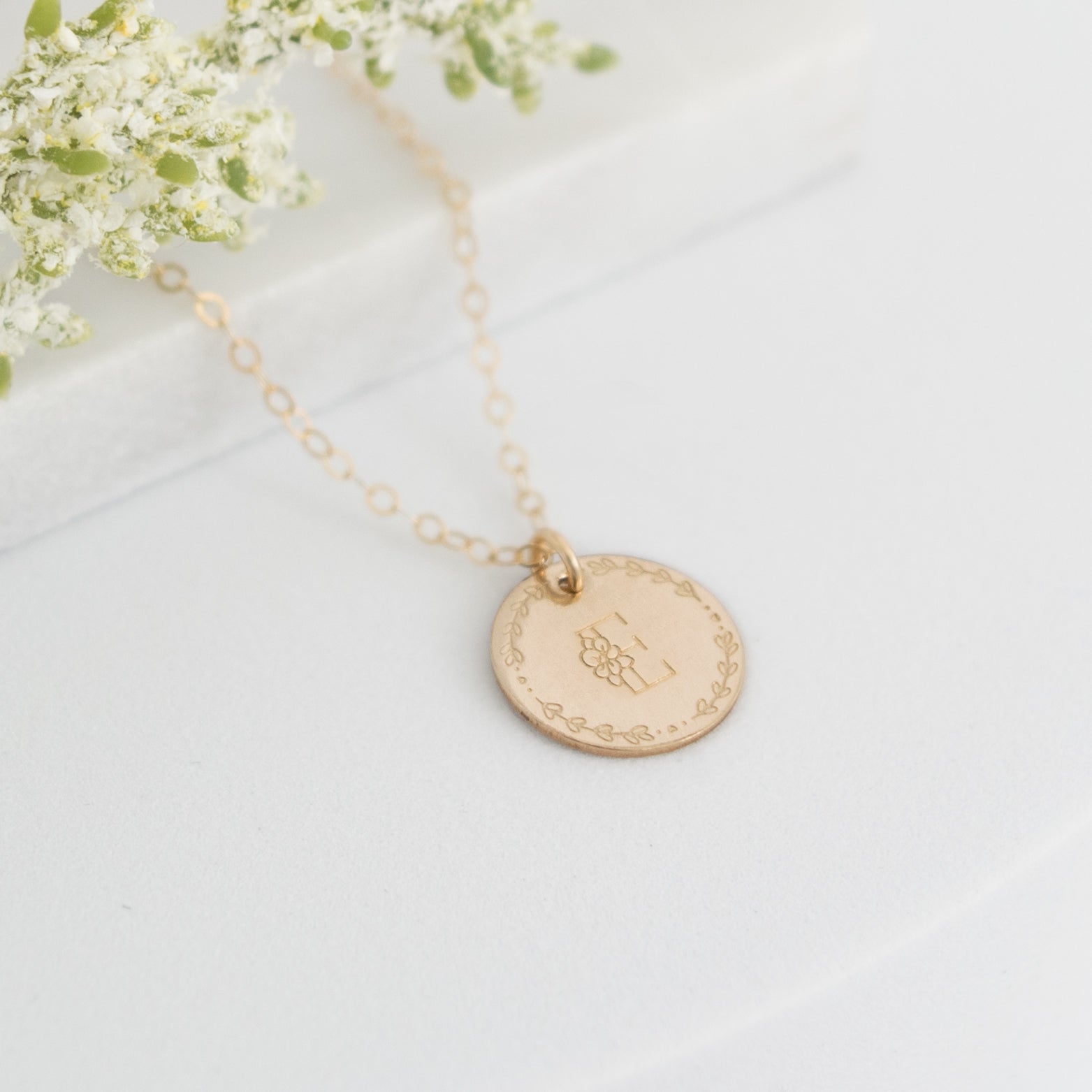 Flora Monogram Necklace featuring a floral initial and wreath design on a ½ inch disc, shown in gold.