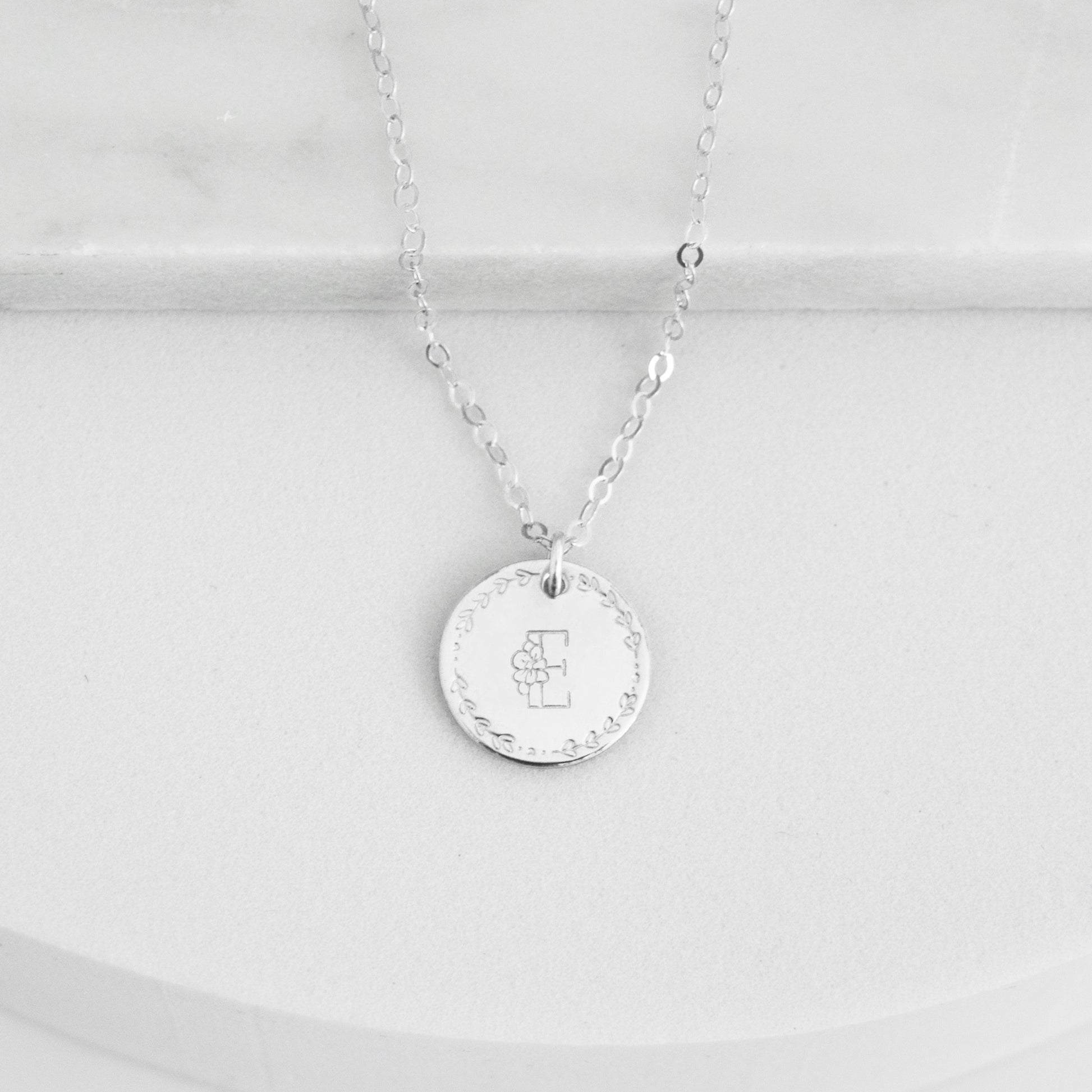 Flora Monogram Necklace featuring a floral initial and wreath design on a ½ inch disc, shown in silver.