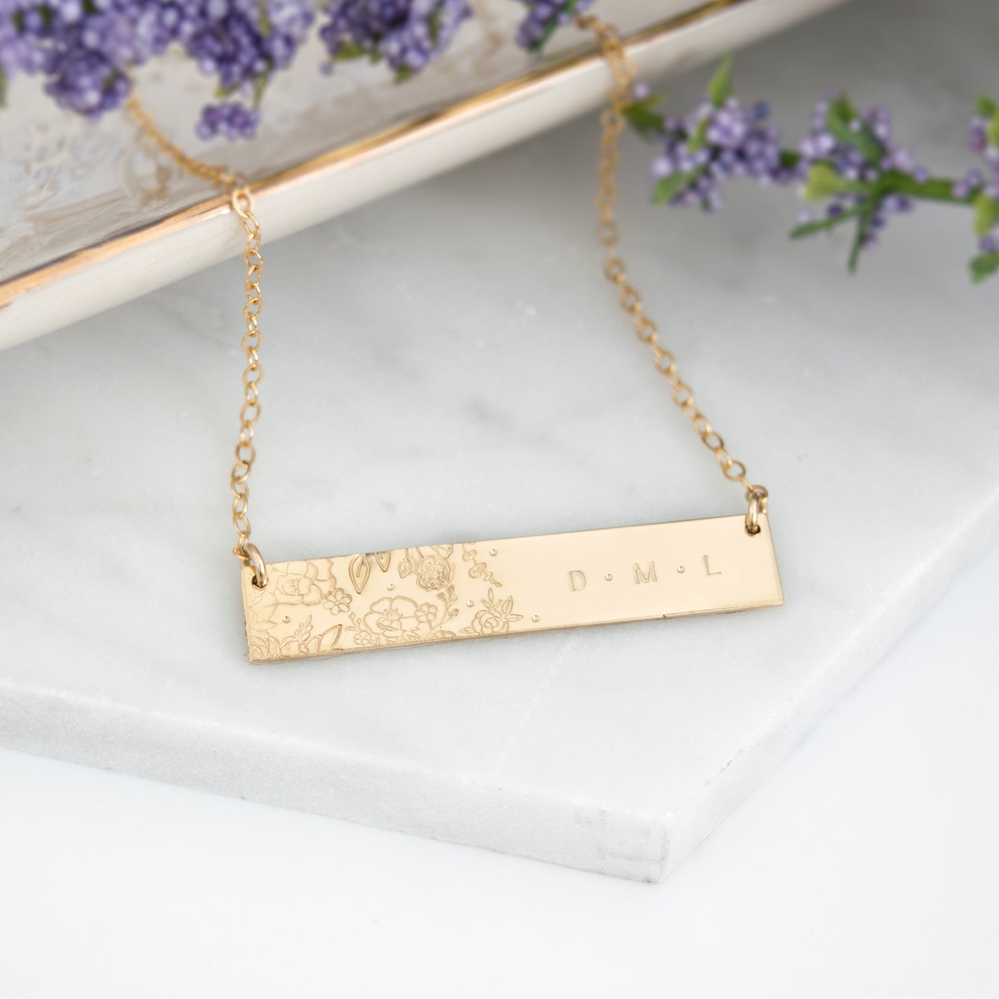 Wild Blooms Bar Necklace featuring a garden of hand-stamped florals and leaves on one side, personalization on the right side. Shown in a flat lay on neutral background.