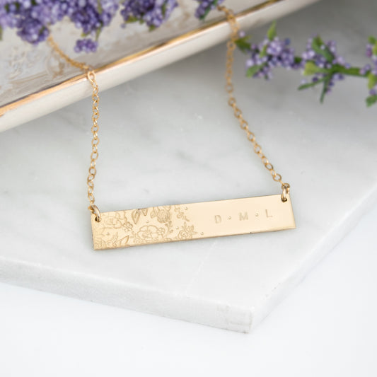 Wild Blooms Bar Necklace featuring a garden of hand-stamped florals and leaves on one side, personalization on the right side. Shown in a flat lay on neutral background.
