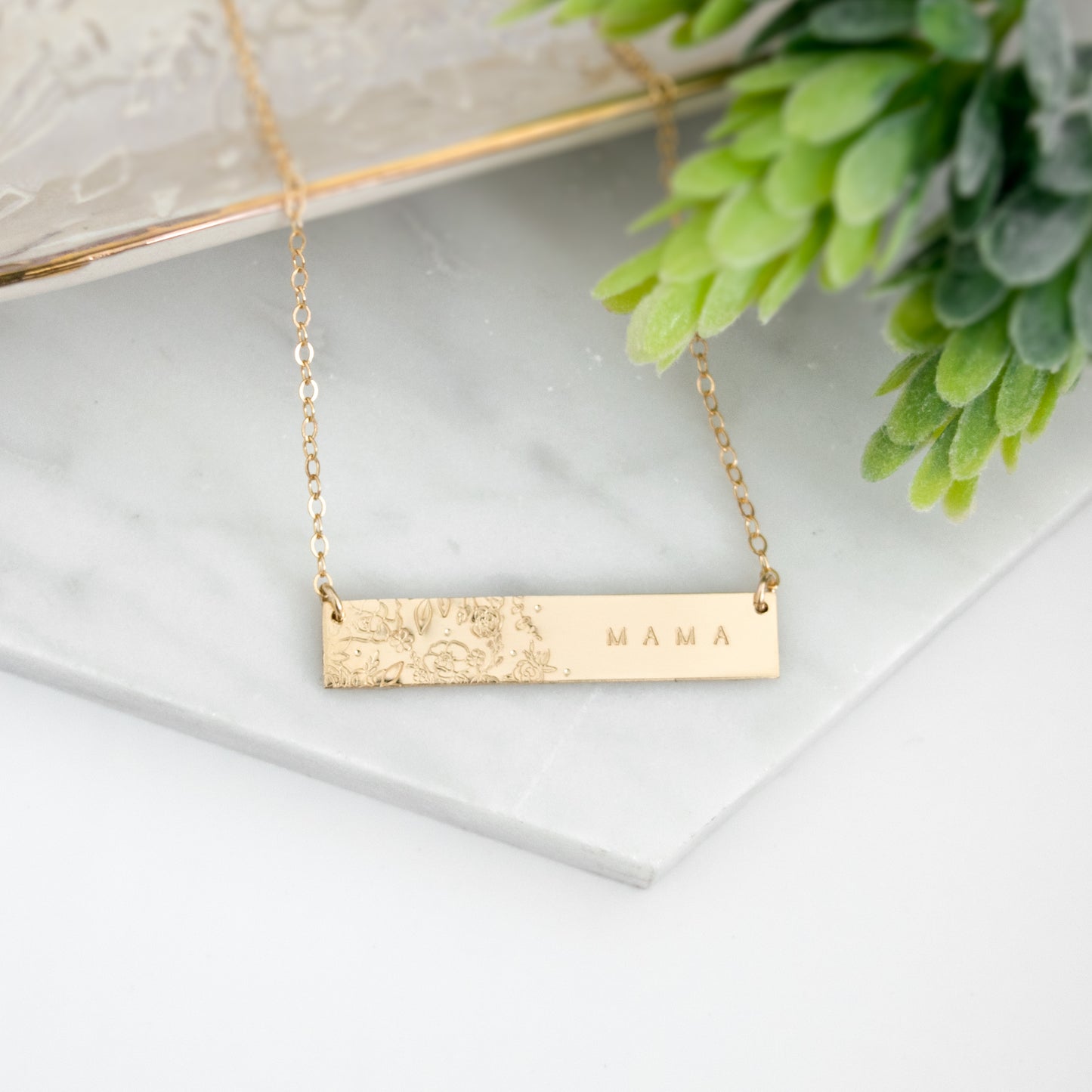 Wild Blooms Bar Necklace featuring a garden of hand-stamped florals and leaves on one side, personalization on the right side. Shown in a flat lay on neutral background.