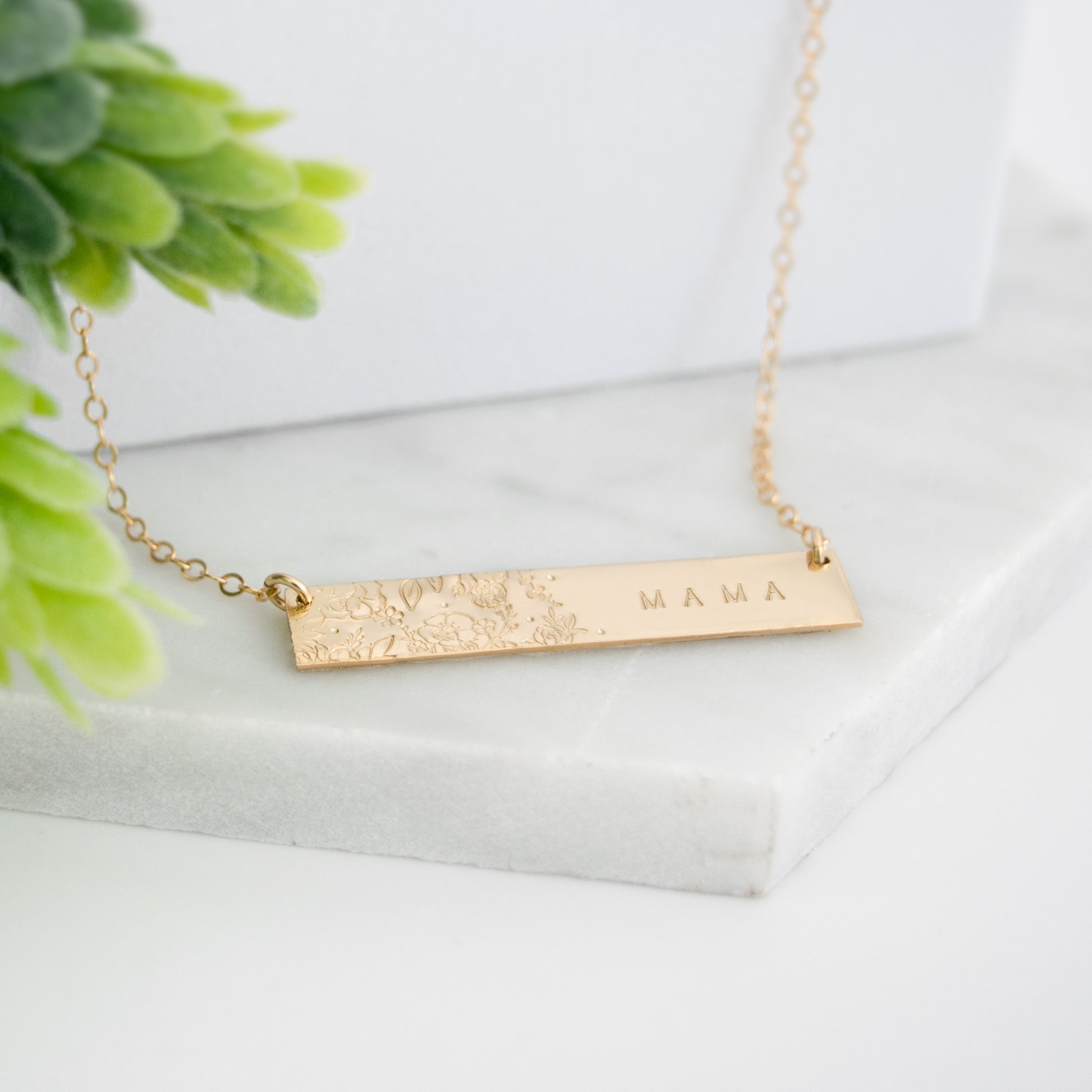 Wild Blooms Bar Necklace featuring a garden of hand-stamped florals and leaves on one side, personalization on the right side. Shown in a flat lay on neutral background.