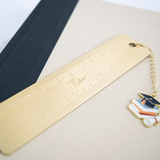 Personalized brass graduation bookmark with hand-stamped name and graduation cap charm.
